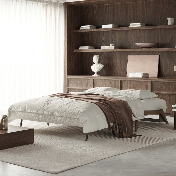 Stretch sofa bed open to a bed and made up with bedding. In a living room with wood walls and shelving